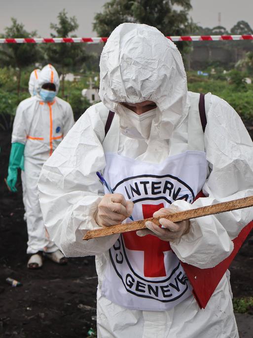 In Schutzanzüge verhüllte Helfer des Internationalen Roten Kreuzes (IRK) bergen die Toten nach Häuserkämpfen in der kongolesischen Millionenstadt Goma. Eine Person steht im Vordergrund, andere arbeiten weiter hinten. 