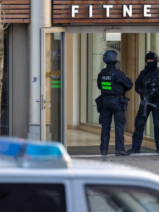 Zu sehen ist der Eingang eines Fitnessstudios in Duisburg. Zwei Polizeibeamte stehen dort nach einer Messerattacke am Eingang.
