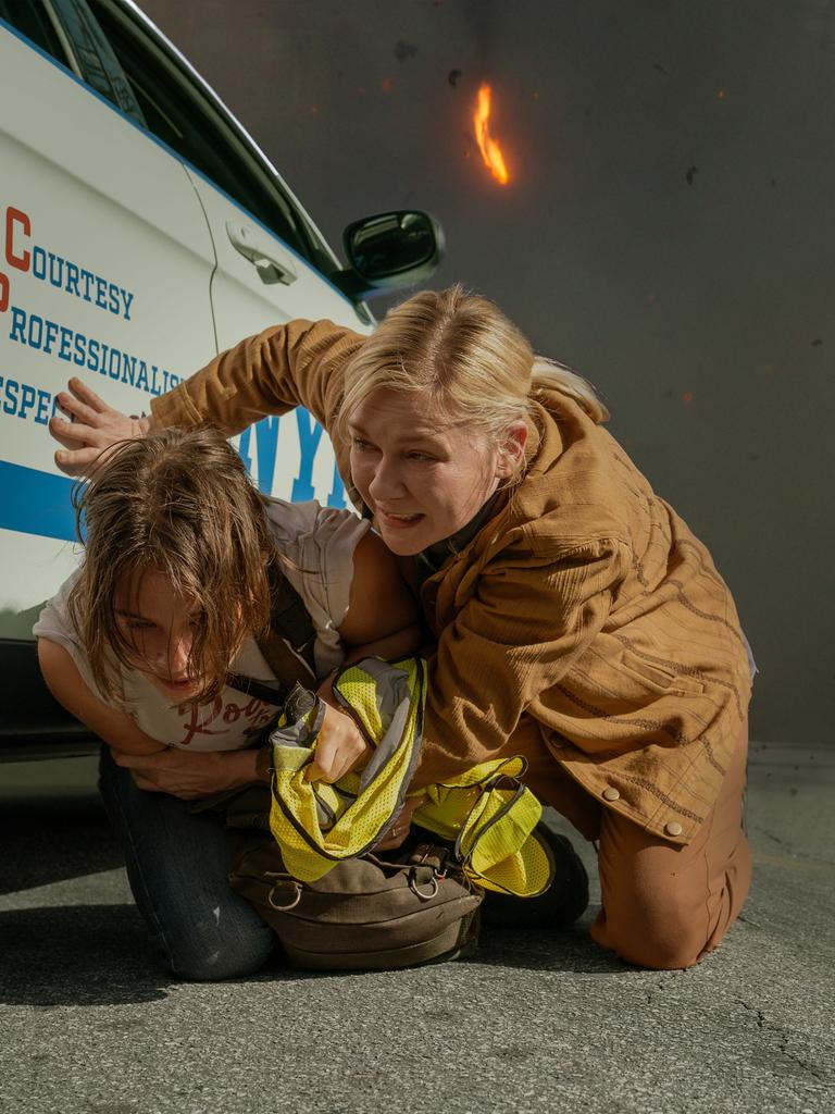 Lee, gespielt von Kirsten Dunst, und Jessie, verkörpert von Cailee Spaeny, ducken sich an der Seite eines Wagens. 