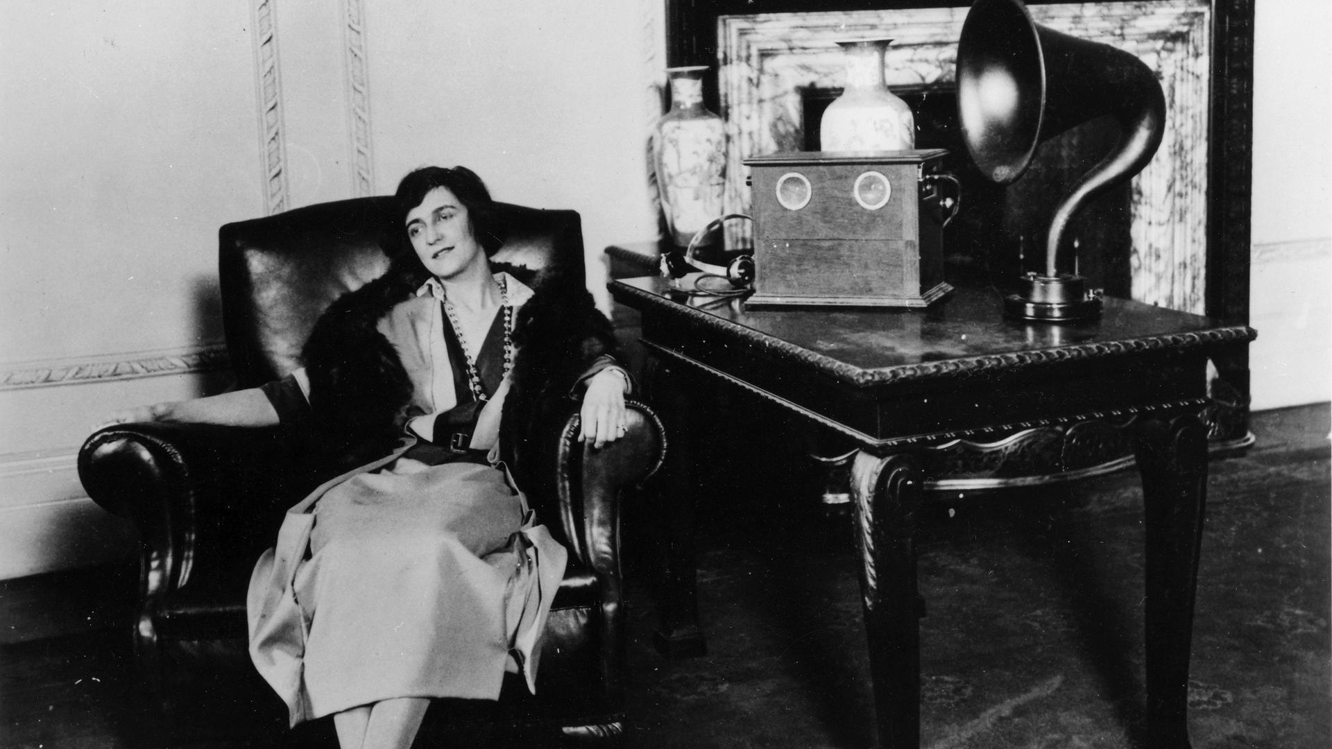 Eine Frau sitzt 1922 in einem Sessel und hört Radio.