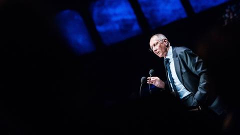 Konrad Paul Liessmann steht auf einem Podium und spricht zu einem Publikum. Er trägt einen grauen Anzug mit Krawatte.