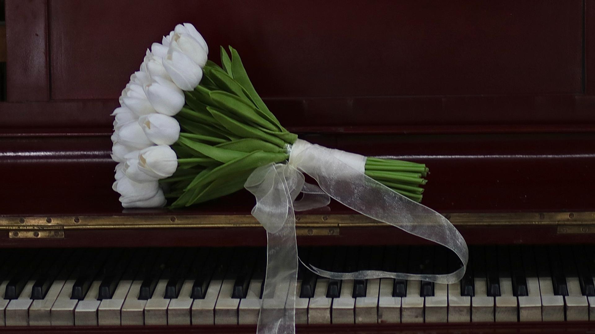 Ein Strauss weißer Tulpen liegt auf einem Klavier.
