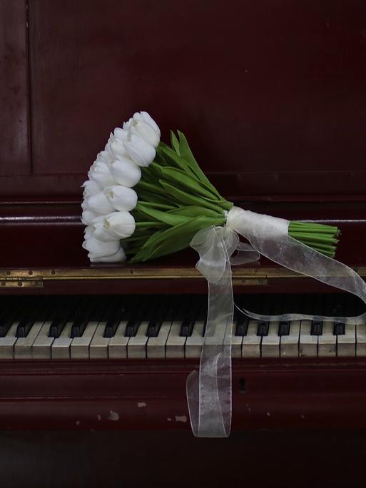 Ein Strauss weißer Tulpen liegt auf einem Klavier.