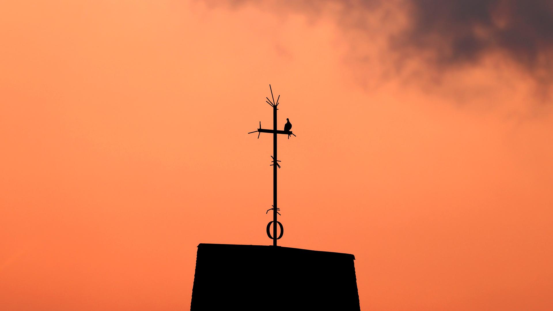 Ein Kreuz steht auf dem Dach einer Kirche vor Abendhimmel. Ein Kreuz steht auf dem Dach einer Kirche vor Abendhimmel.