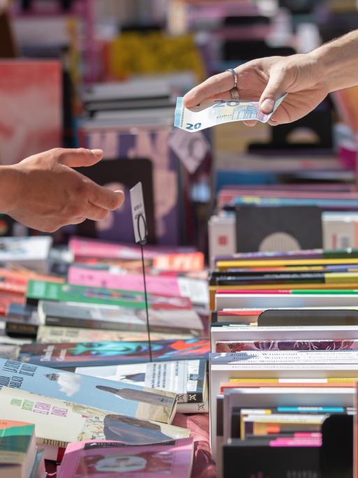 Über einen Tisch voll mit Bücher wird ein 20-Euro-Schein zum Bezahlen gereicht. Über einen Tisch voll mit Bücher wird ein 20-Euro-Schein zum Bezahlen gereicht.