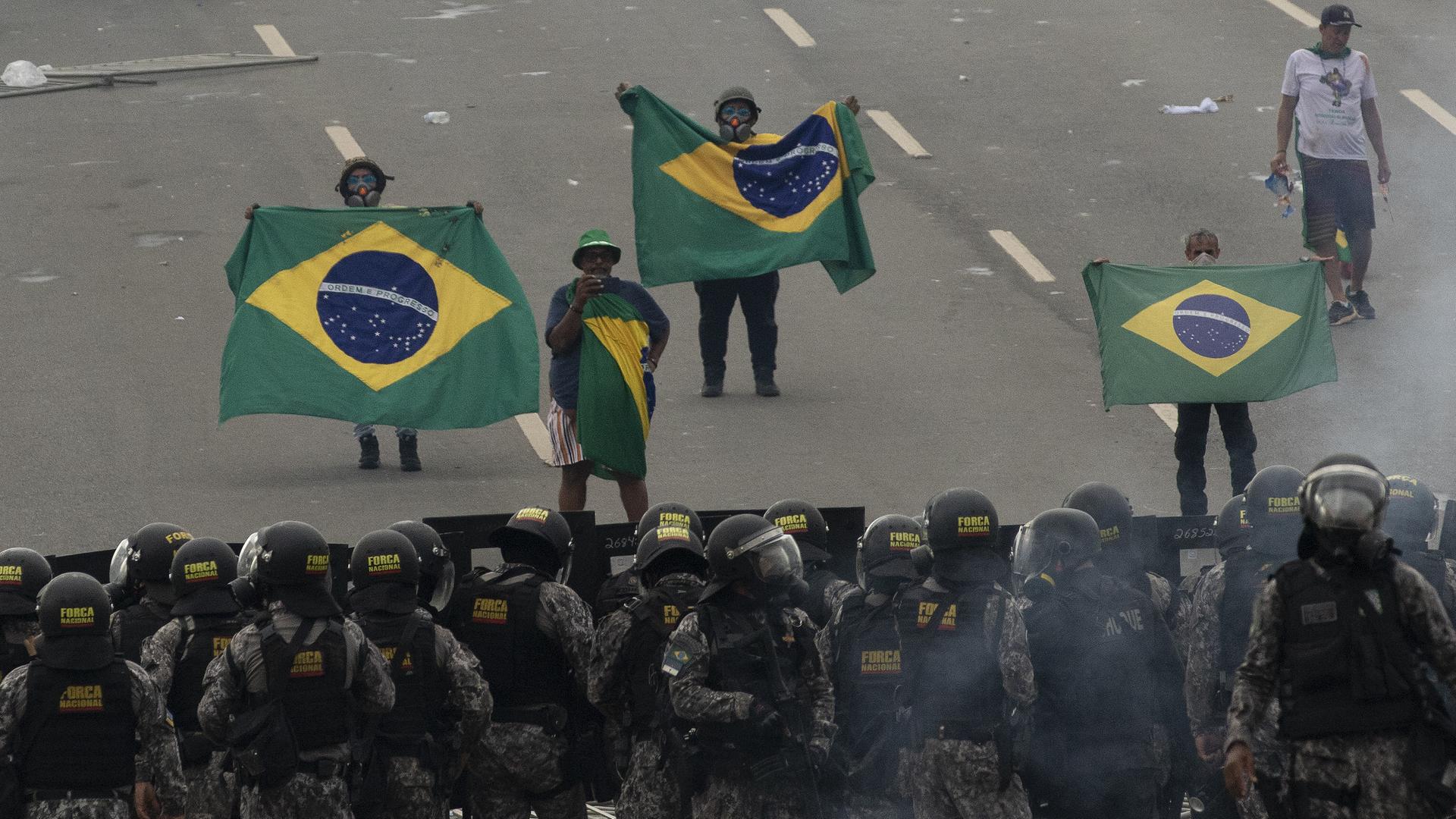 Anhänger des Ex-Präsidenten Bolsonaro stehen, brasilianische Fahnen haltend, Sicherheitskräften gegenüber. Anhänger des Ex-Präsidenten Bolsonaro stehen, brasilianische Fahnen haltend, Sicherheitskräften gegenüber.
