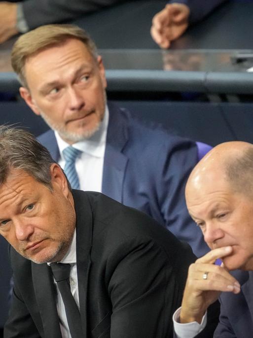 Christian Lindner, Robert Habeck und Olaf Scholz (SPD) sitzen auf der Regierungsbank des Bundestags. Sie blicken in unterschiedliche Richtungen.