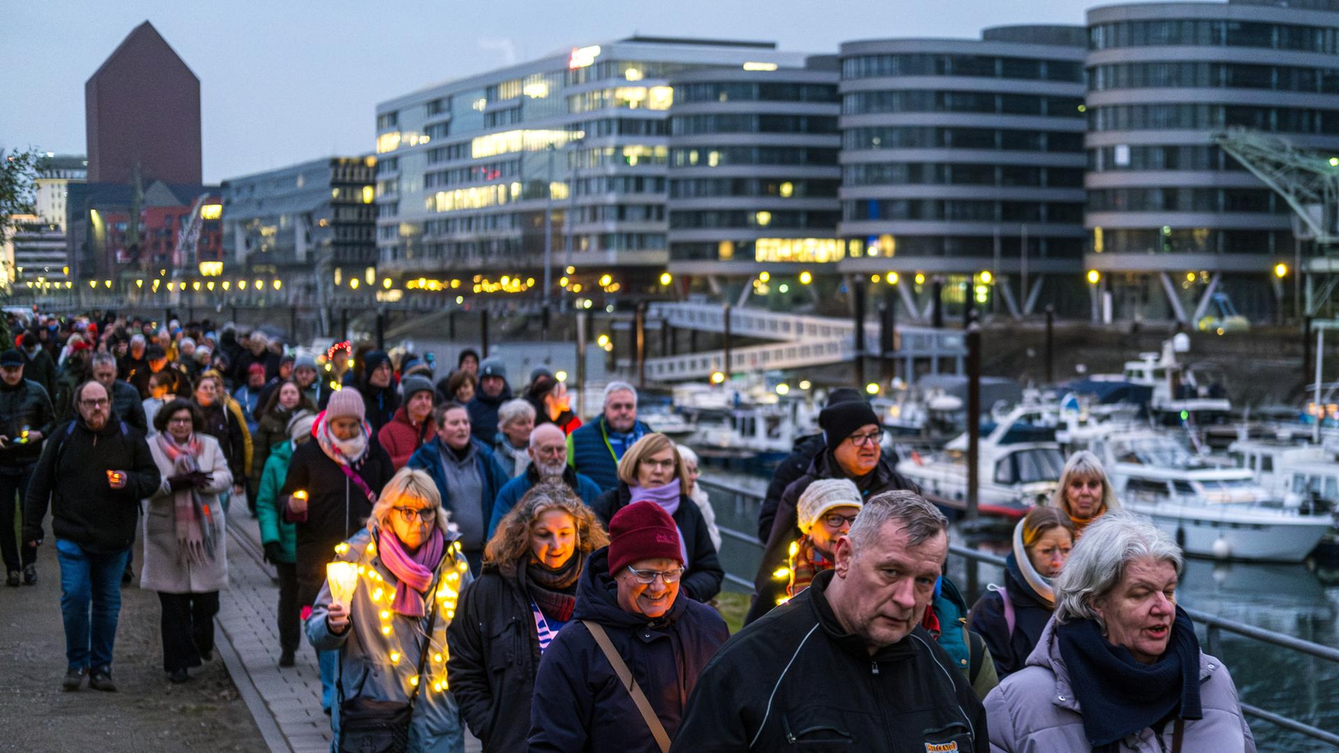 Menschen mit Kerzen in der Hand gehen in der einsetzenden Dämmerung an einem Geländer am Kai des Duisburger Innenhafens entlang, um ein Zeichen gegen Rechtsradikalismus zu setzen. 