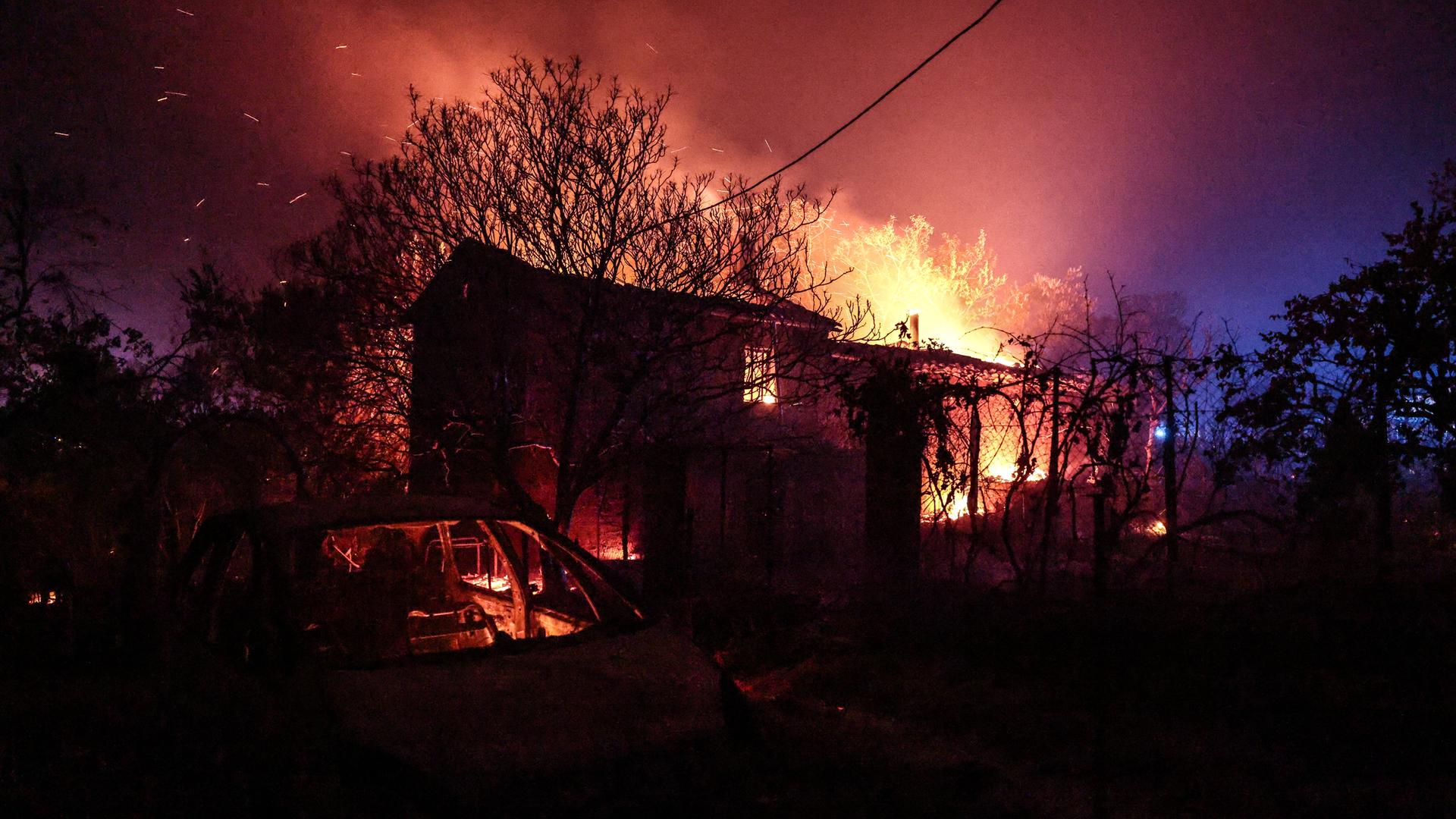 Ein Haus in Cotignac im Südosten Frankreichs wird von einem Feuer zerstört, ein ausgebranntes Auto steht davor, die Flammen lodern im Hintergrund, Juli 2026.