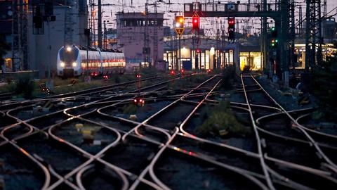 Verzweigte Eisenbahnschienen vor einem Bahnhof, links fährt ein ICE.