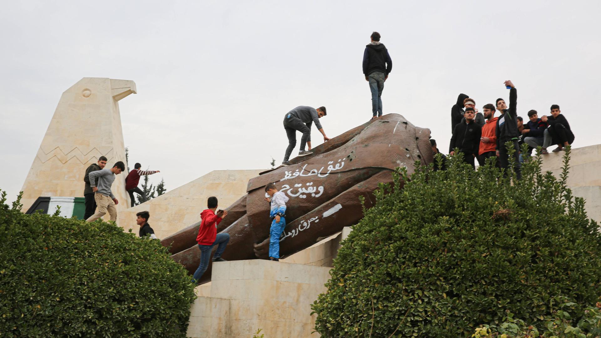 Eine große Anzahl von Kindern posiert vor einer abgerissenen Statue des ehemaligen syrischen Präsidenten Hafez al-Assad in der syrischen Stadt Hama nach dem Vormarsch der syrischen Rebellengruppen unter Führung von Hayat Tahrir al-Sham. 