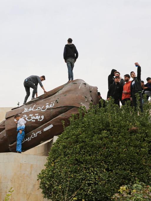 Eine große Anzahl von Kindern posiert vor einer abgerissenen Statue des ehemaligen syrischen Präsidenten Hafez al-Assad in der syrischen Stadt Hama nach dem Vormarsch der syrischen Rebellengruppen unter Führung von Hayat Tahrir al-Sham. 