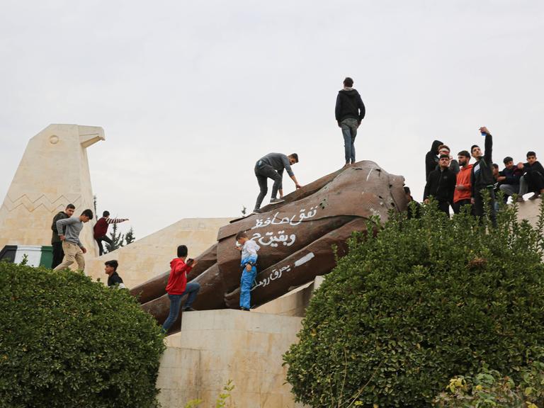 Eine große Anzahl von Kindern posiert vor einer abgerissenen Statue des ehemaligen syrischen Präsidenten Hafez al-Assad in der syrischen Stadt Hama nach dem Vormarsch der syrischen Rebellengruppen unter Führung von Hayat Tahrir al-Sham. 