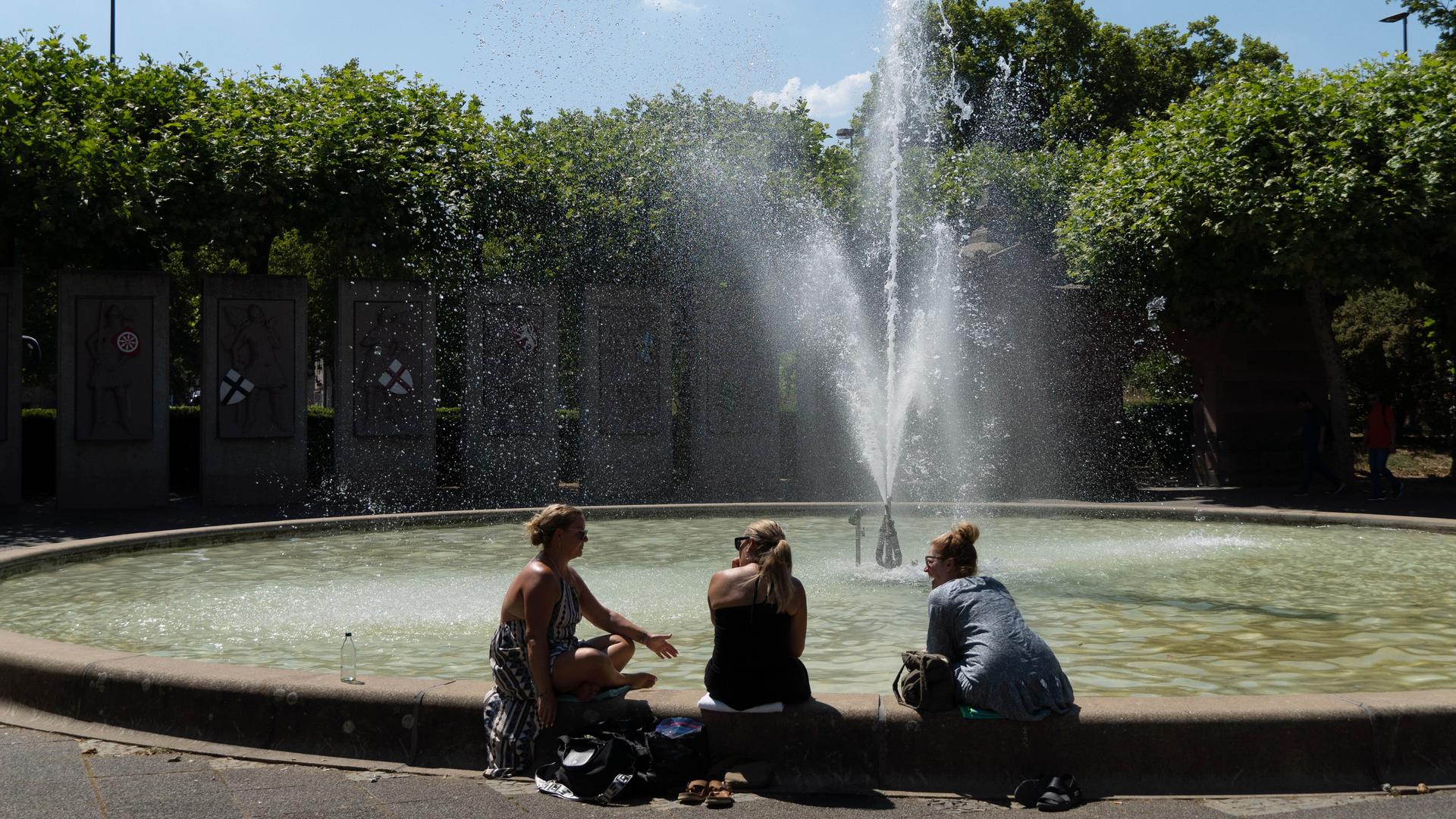 Bei der Hitzewelle im Juli suchen drei Menschen in Mainz Abkühlung an einem Brunnen.