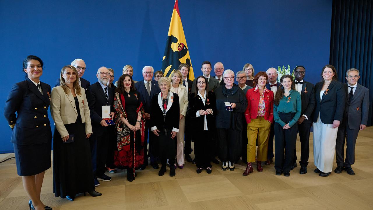 Bundespräsident Steinmeier  und seine Frau Elke Büdenbender stehen zusammen mit Bundestagspräsidentin Julia Klöckner und einer Gruppe von Menschen vor einer blauen Wand.