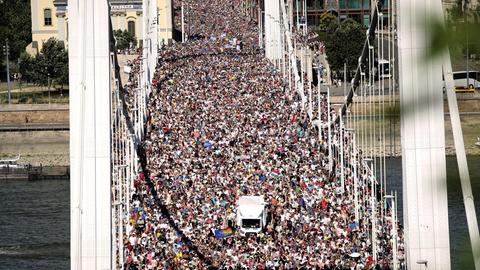Blick auf eine große Brücke in Budapest, die mit Menschen überfüllt ist. Auch die Straße hinter der Brücke ist voller Menschen.
