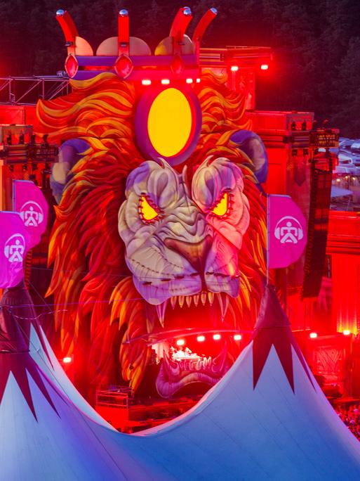 Musikfans tanzen und feiern nach Sonnenuntergang vor einer der Bühnen des "Airbeat One"-Festivals in Mecklenburg-Vorpommern. Die Bühne kommt als großer Löwenkopf daher.
