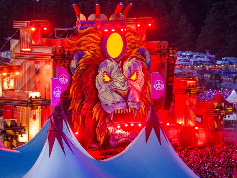 Musikfans tanzen und feiern nach Sonnenuntergang vor einer der Bühnen des "Airbeat One"-Festivals in Mecklenburg-Vorpommern. Die Bühne kommt als großer Löwenkopf daher.