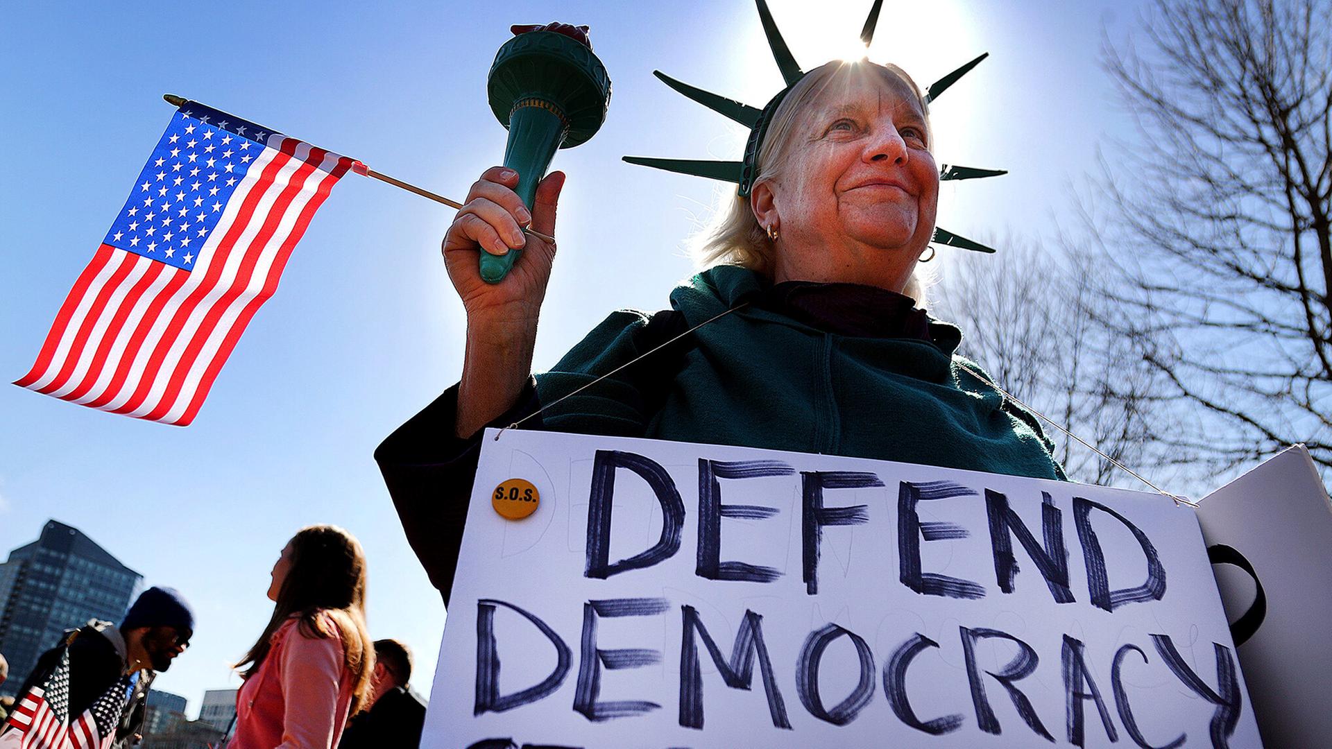 Eine Demonstrantin ist als Freiheitsstatue verkleidet und hält eine US-Flagge.