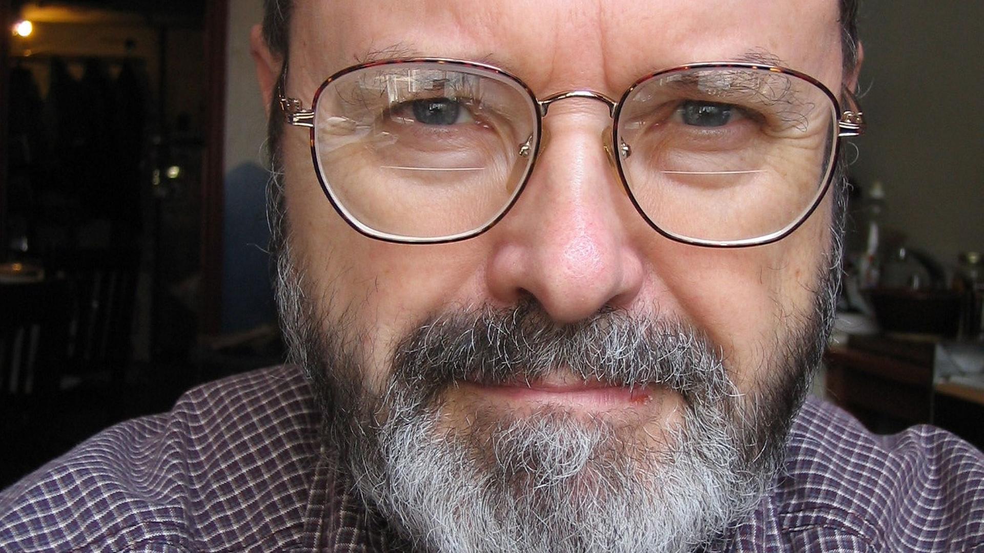 Ein Mann mit großer Brille und silber-schwarzem Bart schaut freundlich in die Kamera