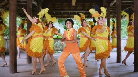 Ein junge in gelb-oranger Kleidung tanzt mit vielen gleichfalls in gelb-orange gekleideten Frauen in einer Pagode.