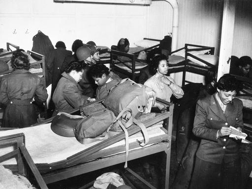 Ein schwarz-weiß-Foto zeigt afro-amerikanische Frauen des Women Army Corps eine Barracke mit Stockbetten beziehen