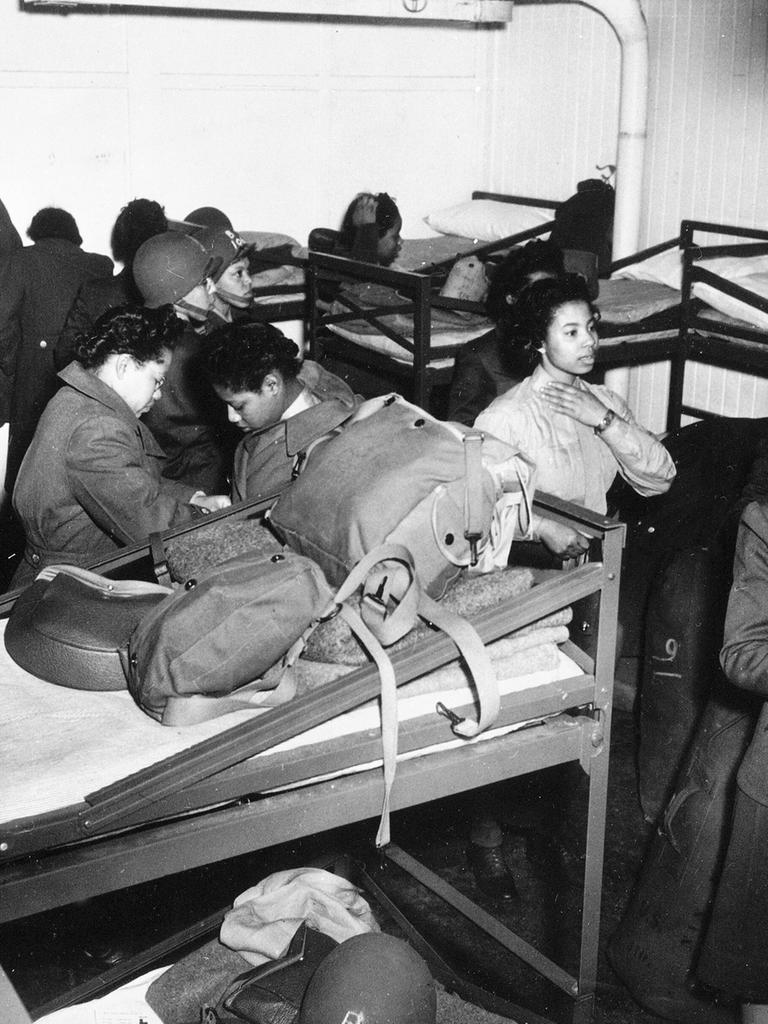 Ein schwarz-weiß-Foto zeigt afro-amerikanische Frauen des Women Army Corps eine Barracke mit Stockbetten beziehen