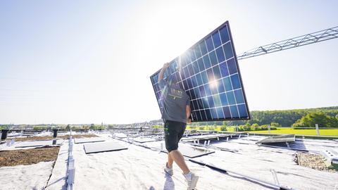 Arbeiter mit Solarpanel vor sonniger Landschaft auf einem Dach