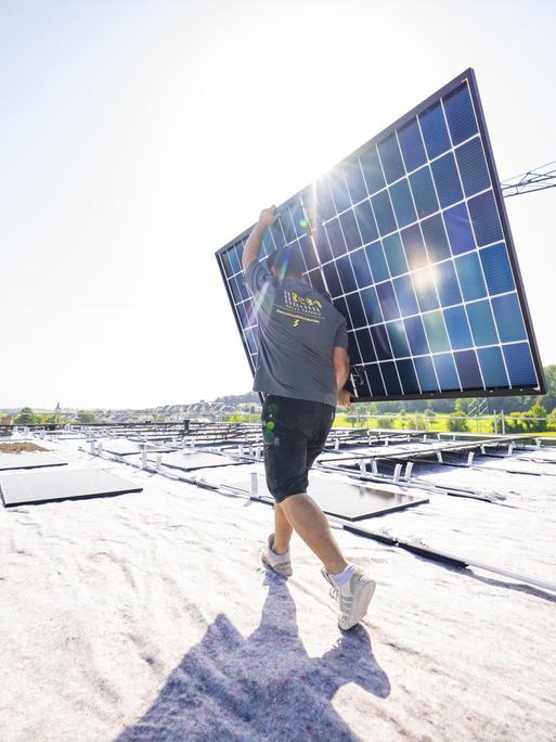 Arbeiter mit Solarpanel vor sonniger Landschaft auf einem Dach