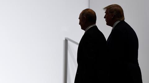 US-Präsident Donald Trump und Russlands Präsident Wladimir Putin stehen dicht beieinander vor einer weißen Wand. Sie sind im Profil und im Halbschatten abgebildet. 