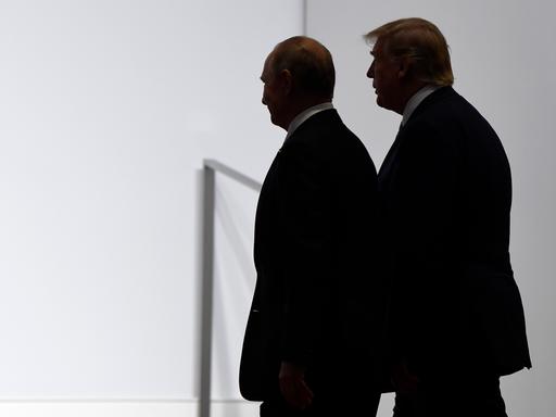 US-Präsident Donald Trump und Russlands Präsident Wladimir Putin stehen dicht beieinander vor einer weißen Wand. Sie sind im Profil und im Halbschatten abgebildet. 