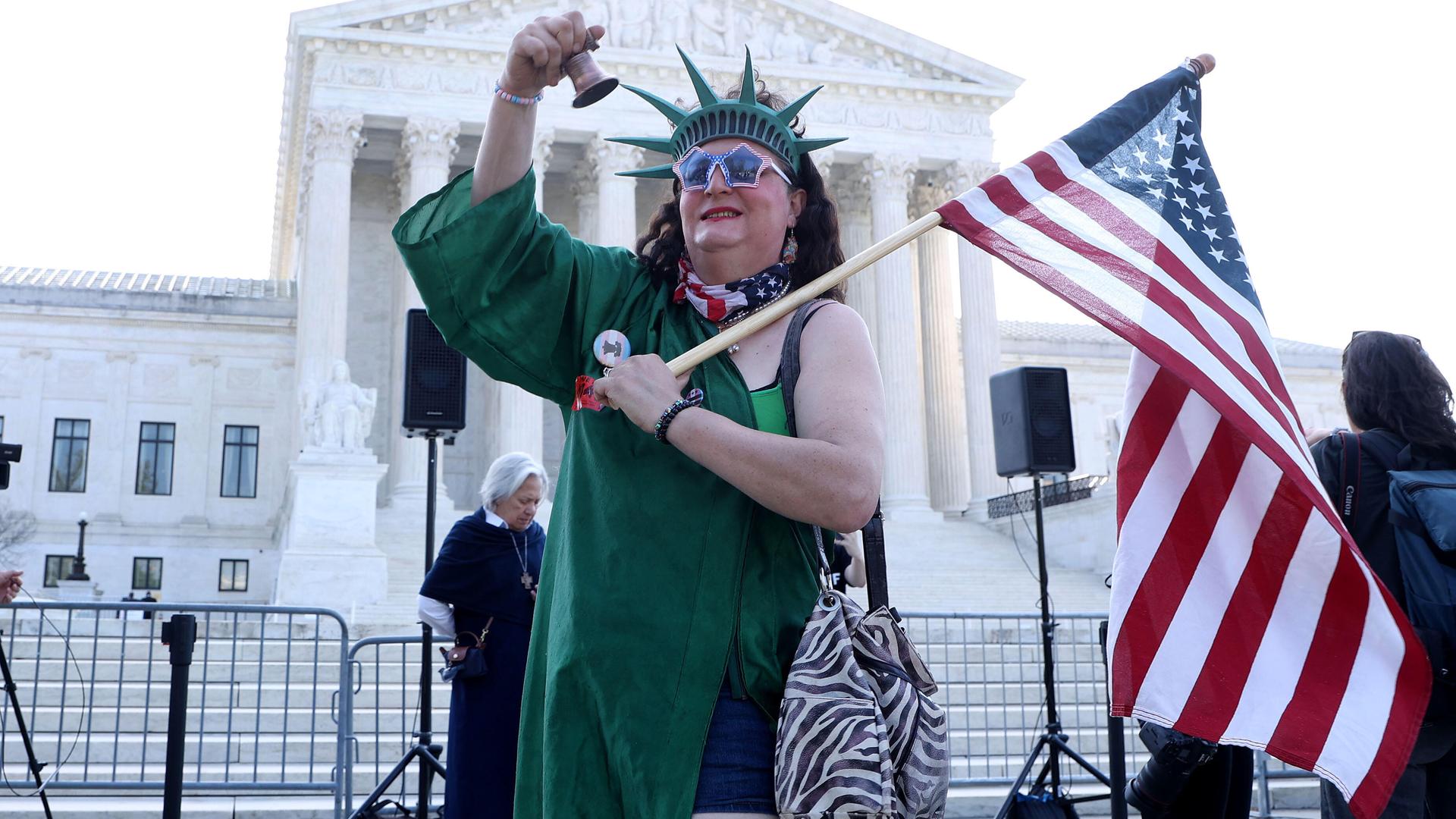 Eine als Freiheitsstatue verkleidete Person läutet eine Glocke während einer Kundgebung zur Unterstützung des Geburtsortsprinzips vor dem Obersten Gerichtshof der USA.