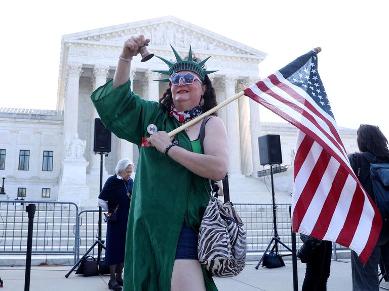 Eine als Freiheitsstatue verkleidete Person läutet eine Glocke während einer Kundgebung zur Unterstützung des Geburtsortsprinzips vor dem Obersten Gerichtshof der USA.