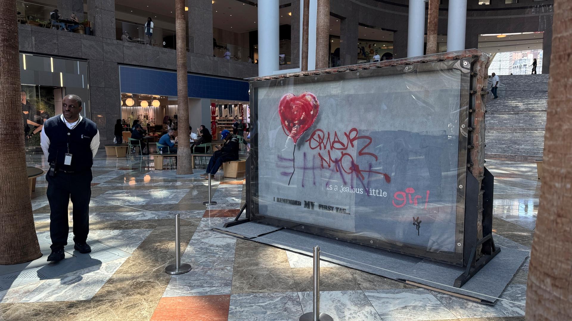 Der Teil der Mauer, die das Kunstwerk trägt, steht in einer großen Halle in New York. Der Teil der Mauer, die das Kunstwerk trägt, steht in einer großen Halle in New York.