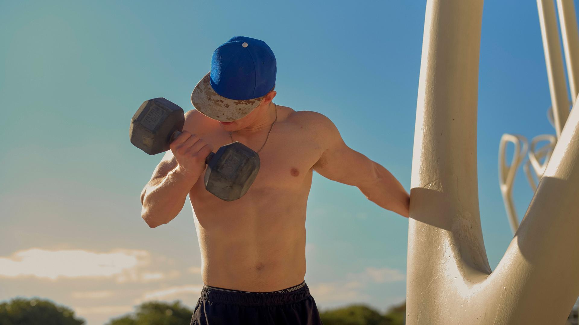 Ein Mann ohne Shirt trainiert mit einer großen Hantel im Freien.