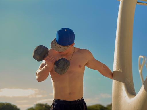 Ein Mann ohne Shirt trainiert mit einer großen Hantel im Freien. Ein Mann ohne Shirt trainiert mit einer großen Hantel im Freien.