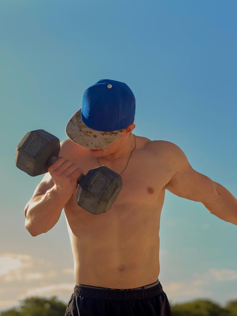 Ein Mann ohne Shirt trainiert mit einer großen Hantel im Freien. Ein Mann ohne Shirt trainiert mit einer großen Hantel im Freien.