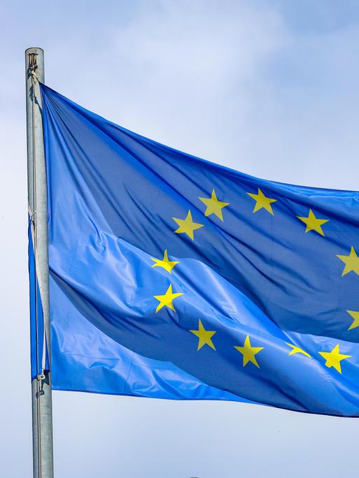 Eine EU-Flagge, die 12 Sterne auf blauem Grund zeigt, weht an einem Fahnenmast im Wind. 