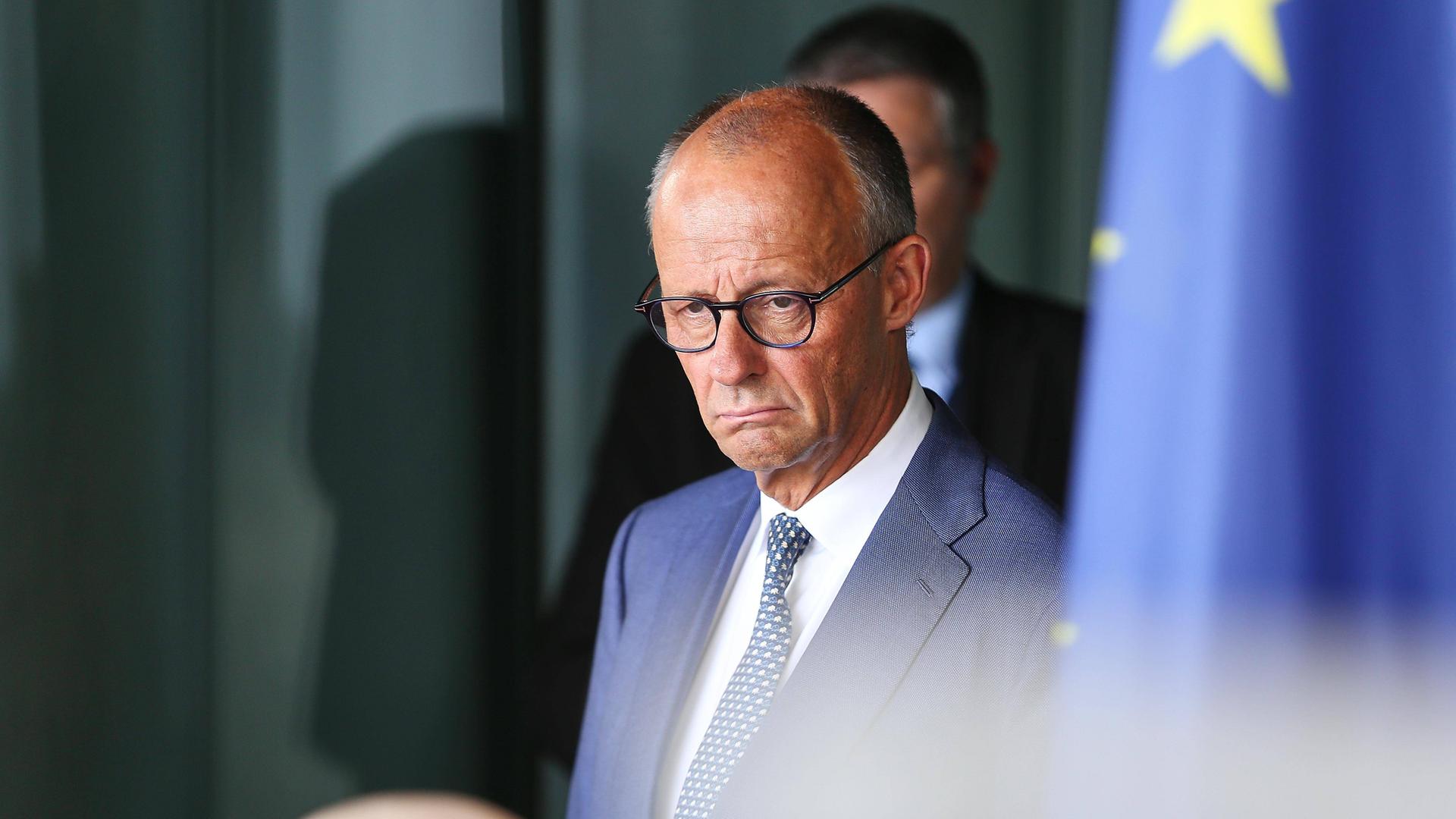 Friedrich Merz im Kanzleramt. er guckt etwas mürrisch. Rechts von ihm ist auf dem Bild etwas unscharf eine Europafahne zu sehen. Friedrich Merz im Kanzleramt. er guckt etwas mürrisch. Rechts von ihm ist auf dem Bild etwas unscharf eine Europafahne zu sehen.