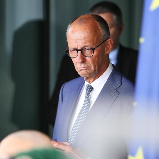 Das Bild zeigt Friedrich Merz im Kanzleramt. Neben ihm ist auf dem Bild etwas unscharf eine Europafahne zu sehen.