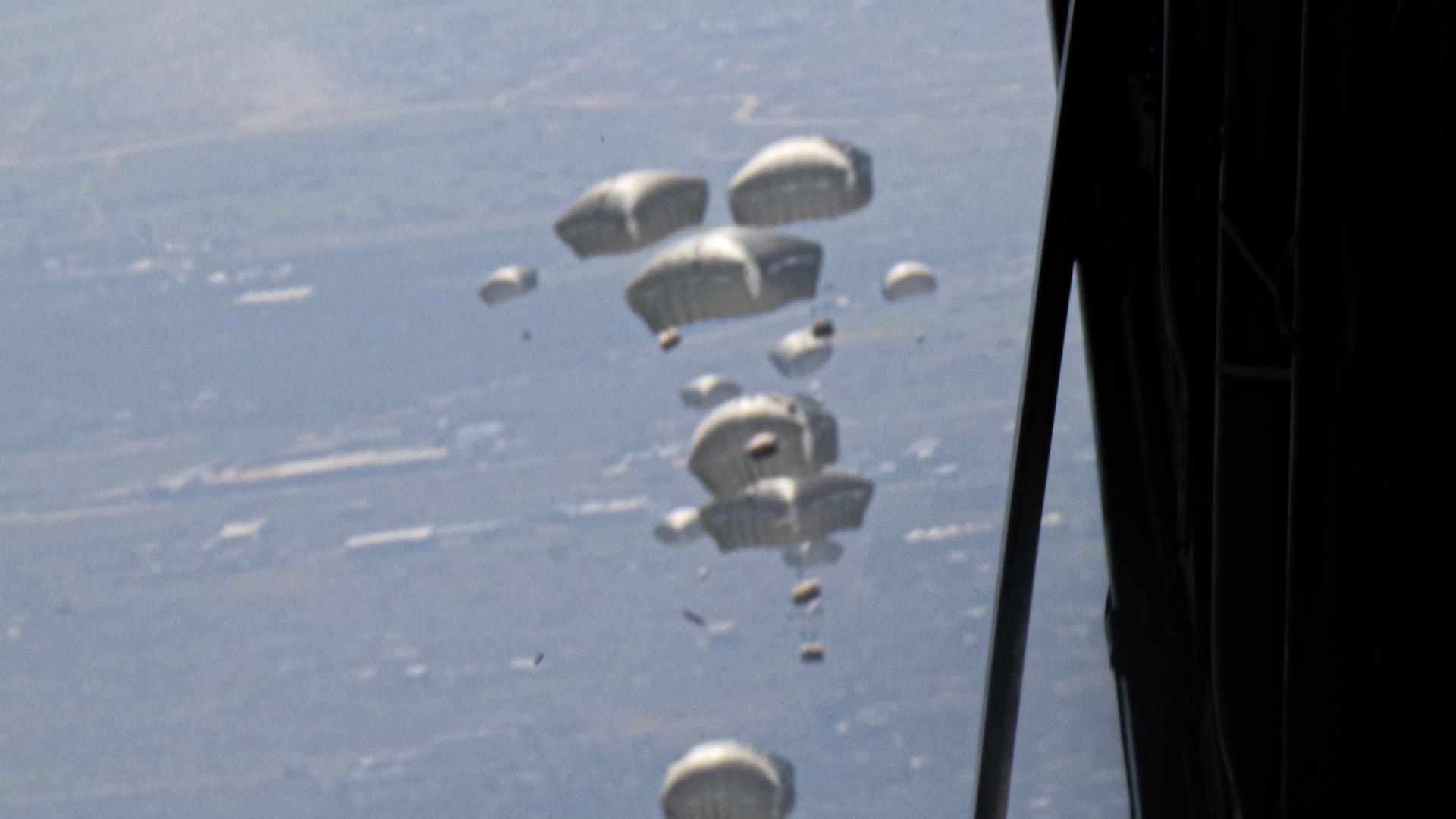 Die Sicht aus einem Flugzeug auf abgeworfene Hilfslieferungen an Fallschirmen in der Luft Die Sicht aus einem Flugzeug auf abgeworfene Hilfslieferungen an Fallschirmen in der Luft