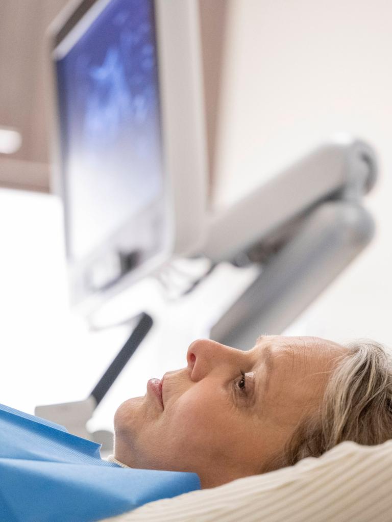 Eine Frau liegt während einer Untersuchung in einem Krankenbett, über ihr an der Wand hängt ein Monitor.