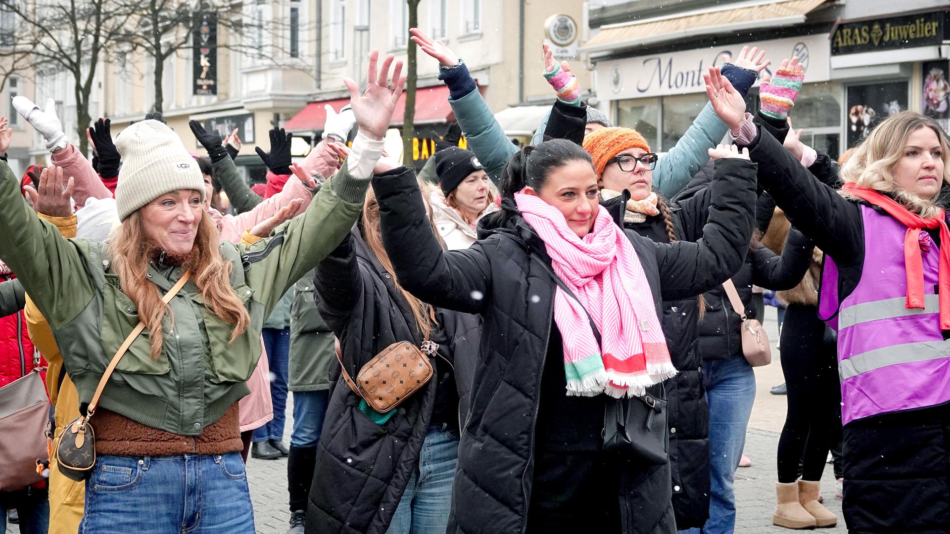 Frauen tanzen auf der One Billion Rising -Aktion vor dem City Center auf der Bahnhofstraße in Herne gegen Gewalt an Frauen und Mädchen. Auf dem Bild sind drei Frauen mit erhobenen Armen im Vordergrund. 