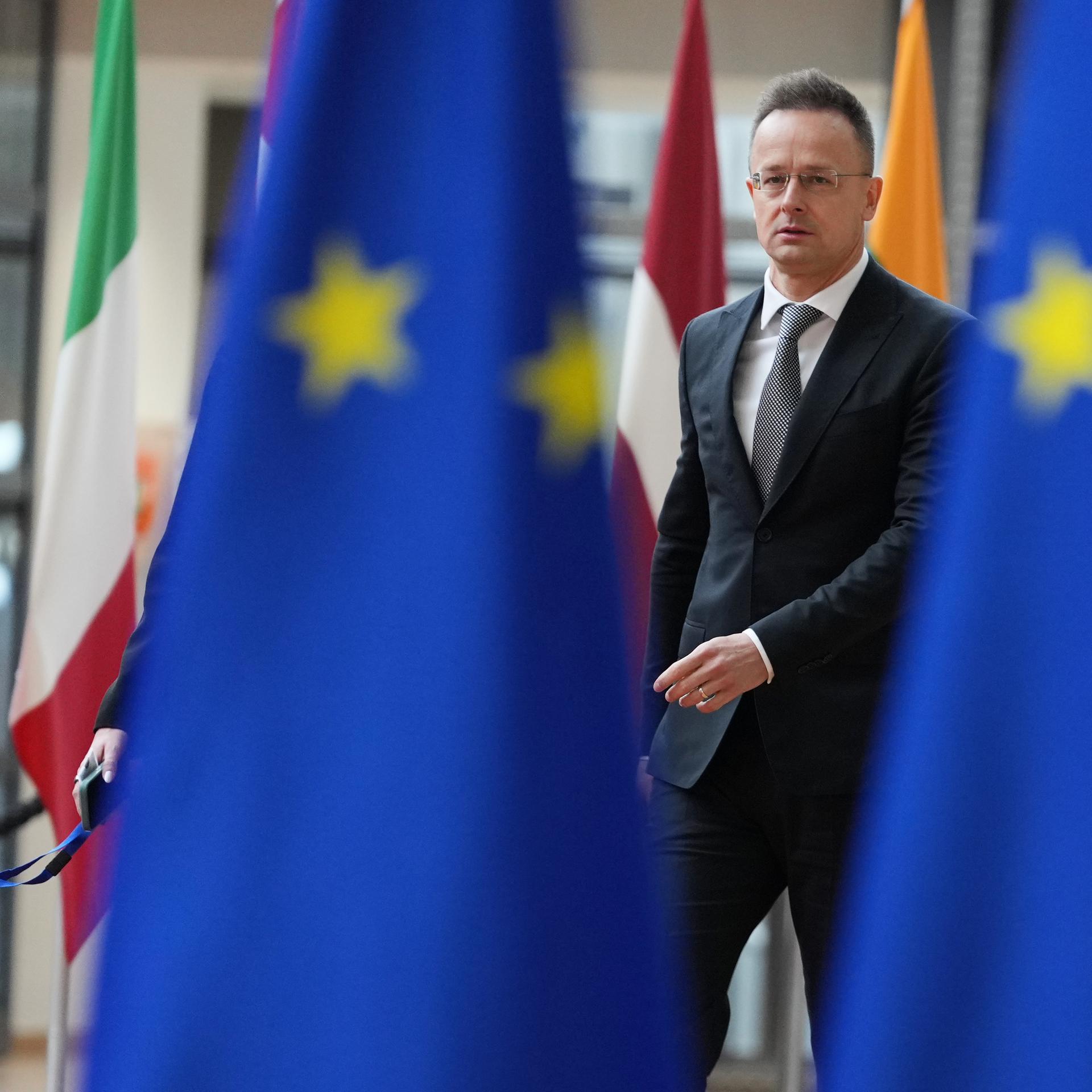 Der ungarische Außenminister Peter Szijjarto trifft zu einem Treffen der EU-Außenminister im Gebäude des Europäischen Rates in Brüssel ein. Um ihn herum sind mehrere Flaggen Europas und der EU. 