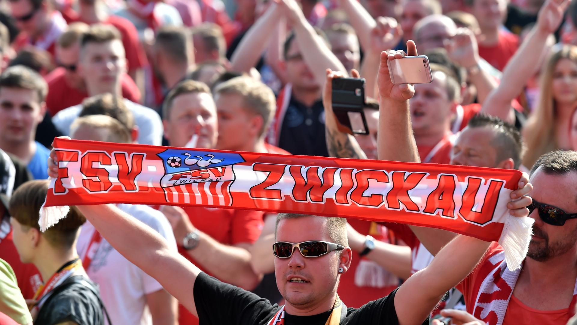 Fußballfans des FSV Zwickau. Ein Fan mit Sonnenbrille hält einen Schal mit der Aufschrift "FSV Zwickau" hoch.