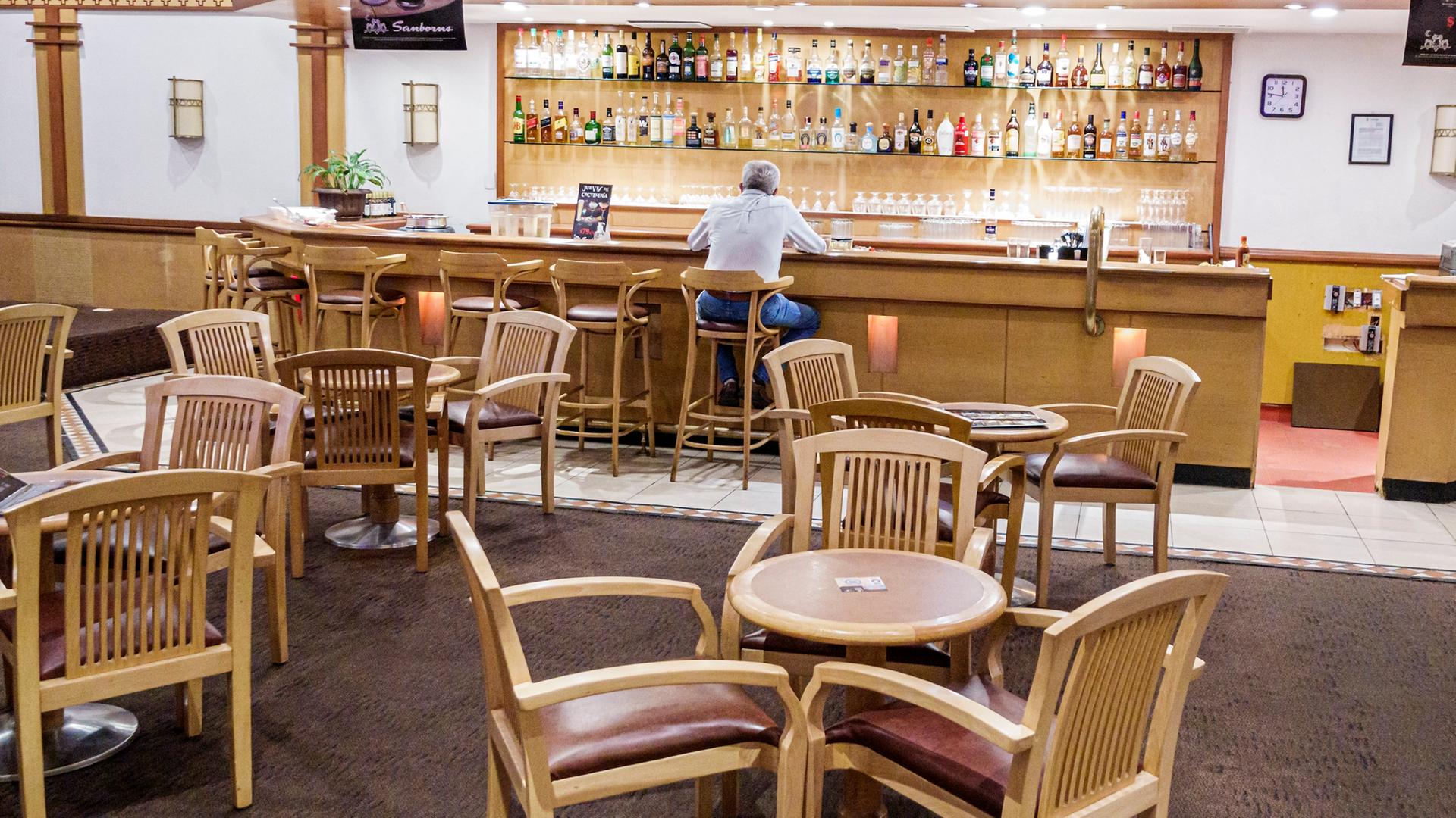 Ein Mann sitzt allein an der Bar eines Restaurants, er ist nur von hinten zu sehen.