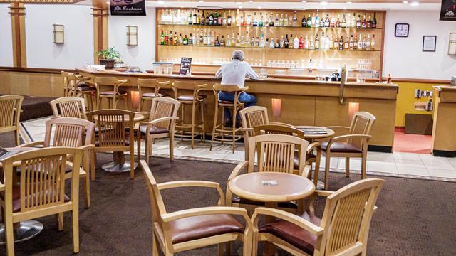 Ein Mann sitzt allein an der Bar eines Restaurants, er ist nur von hinten zu sehen.