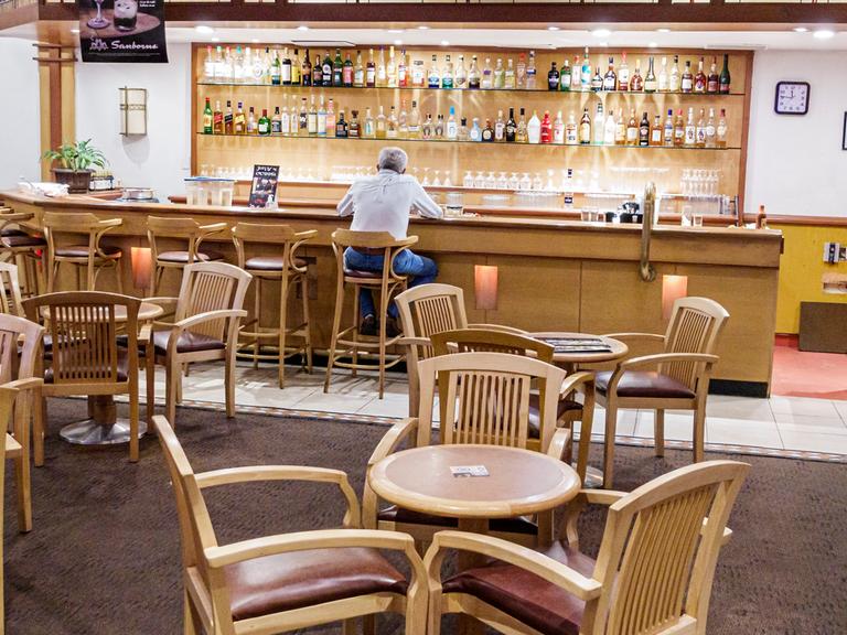 Ein Mann sitzt allein an der Bar eines Restaurants, er ist nur von hinten zu sehen.