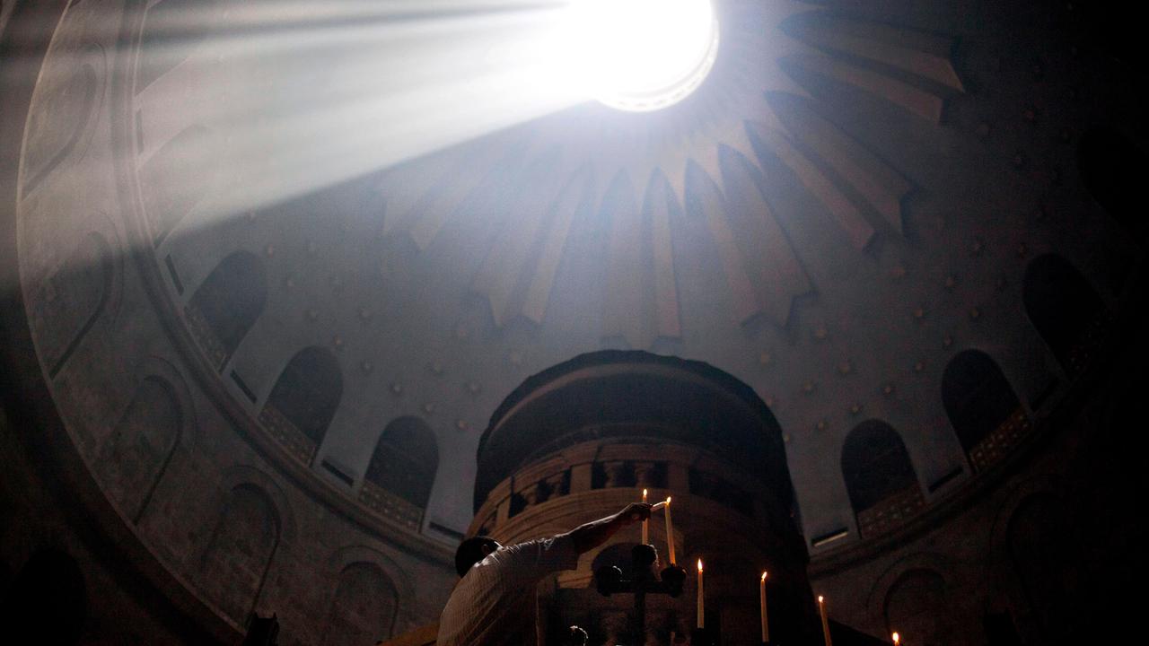 Gläubige entzünden Kerzen an Ostern in der Grabeskirche in Jerusalem. Durcheine Öffnung in der Decke erleuchtet ein Sonnenstrahl den dunklen Raum.