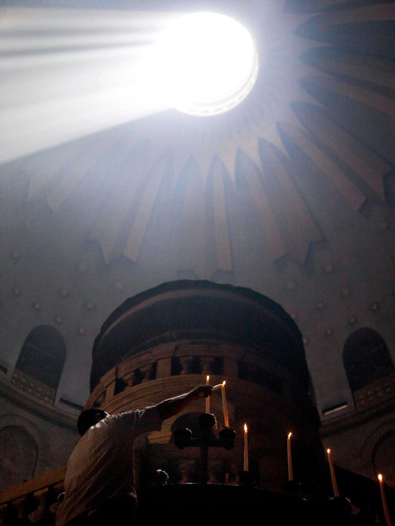 Gläubige entzünden Kerzen an Ostern in der Grabeskirche in Jerusalem. Durcheine Öffnung in der Decke erleuchtet ein Sonnenstrahl den dunklen Raum.